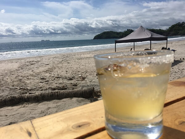 A tasty Coco Loco margarita sits on the edge of the table with the beach and Pacific ocean in the background.