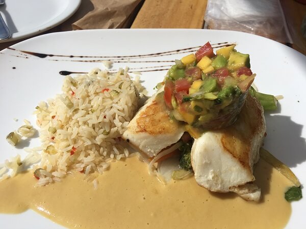 A large price of Corvina with an avocado, mango and tomato salsa on top alongside rice and a beurre blanc sauce.