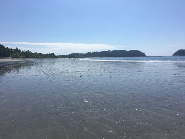 Looking towards the southern portion of Samara beach, the beach is shallow and the sand is dark.