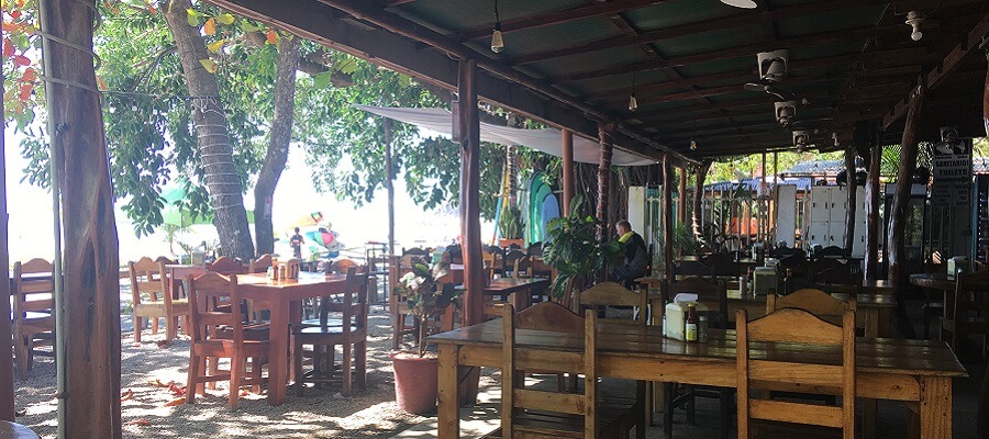 The outdoor dining area at Sheriff Rustic in Samara has a selection of tables under the porch cover or under the trees.