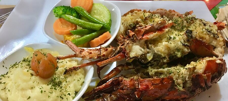Three half lobsters with a garlic butter sauce along with mashed potatoes and steamed vegetables.