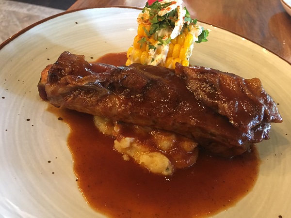 A juicy pork rib on top of homemade mashed potatoes and a slice of tender corn.